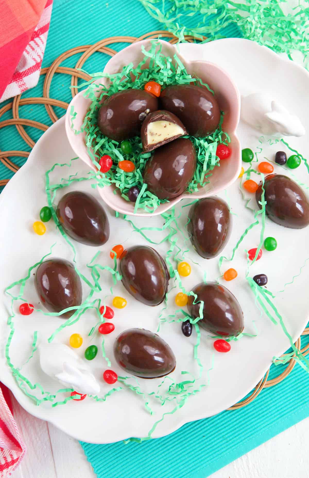 Chocolate eggs on a white platter with a bowl filled with easter grass and more chocolate eggs.