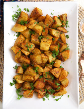 A rectangular serving plate is topped with crispy breakfast potatoes.