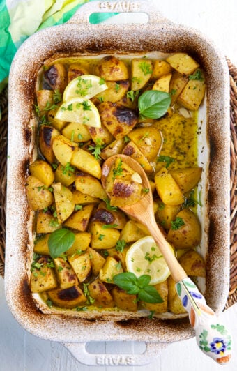 Herbs and lemons garnish a baking dish filled with potatoes.