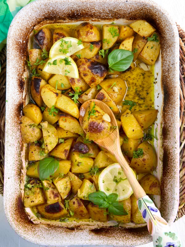 Herbs and lemons garnish a baking dish filled with potatoes.