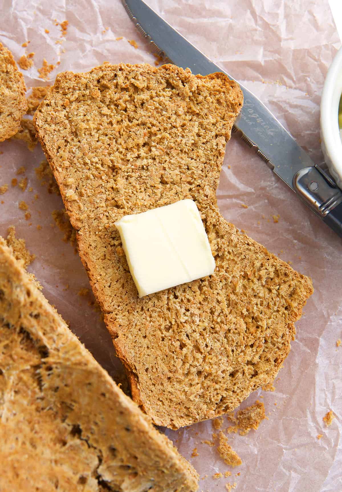 A single piece of brown bread has a square of butter on it.
