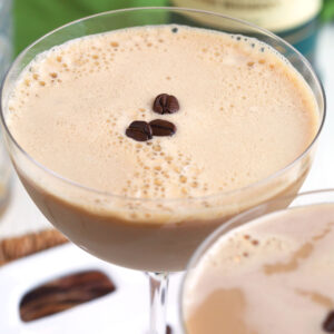 Several coffee beans are placed on top of an espresso martini.