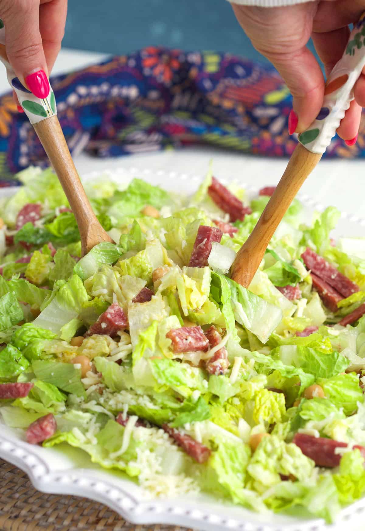 Salad is being tossed with wooden utensils. 
