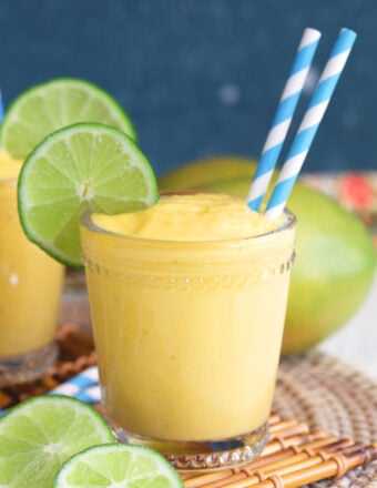 Mango Smoothie with a two blue and white striped straws in a glass with a lime wheel on the side.