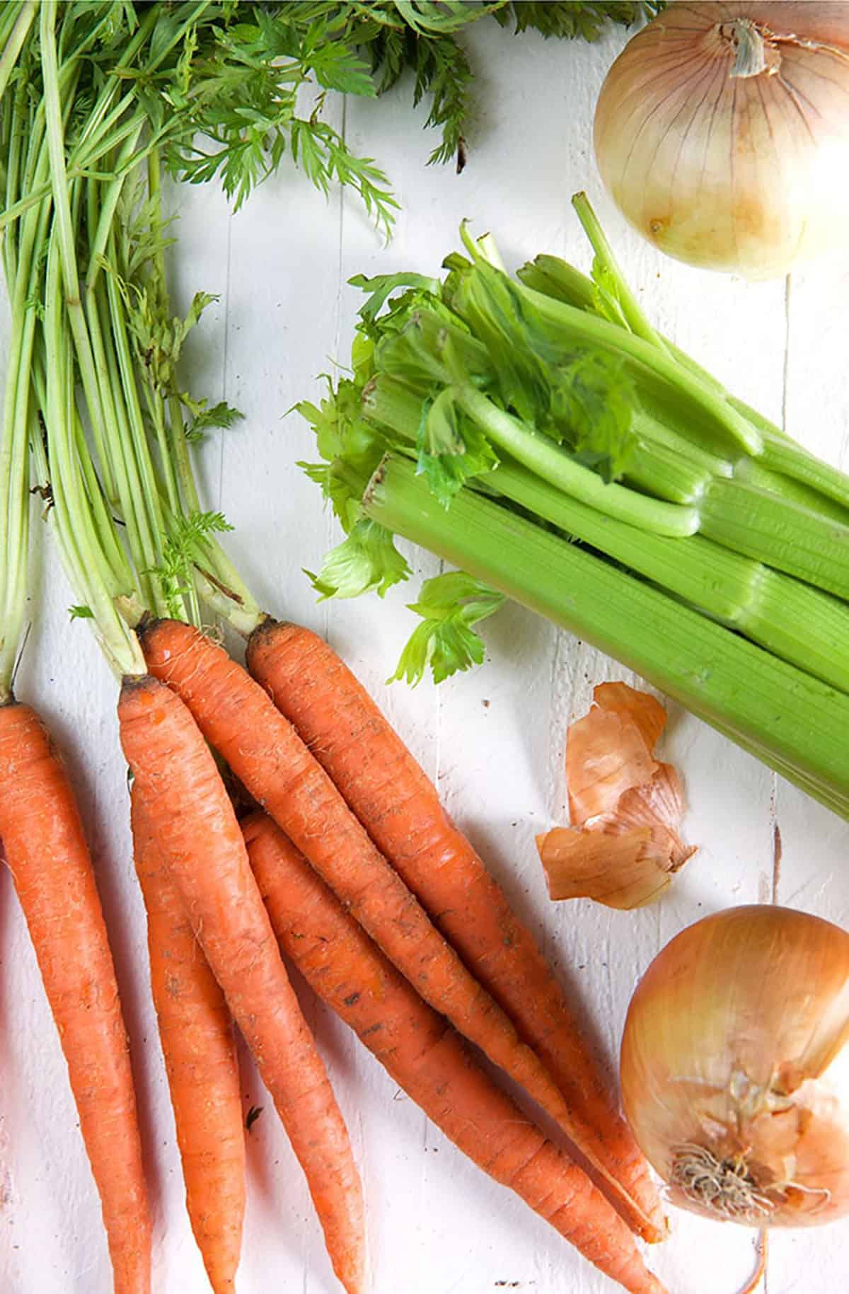 Onions, celery and carrots are being stirred in a large skillet with a wooden spoon.