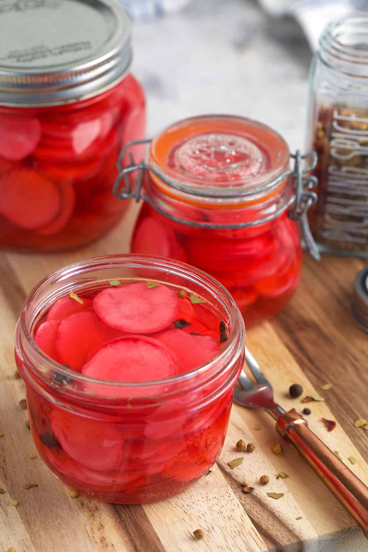 Three jars of pickled radish are placed on a wooden surface. 