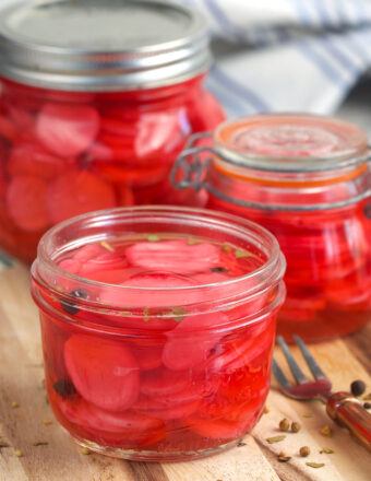 Several jars of pickled radishes are placed on a wooden surface.