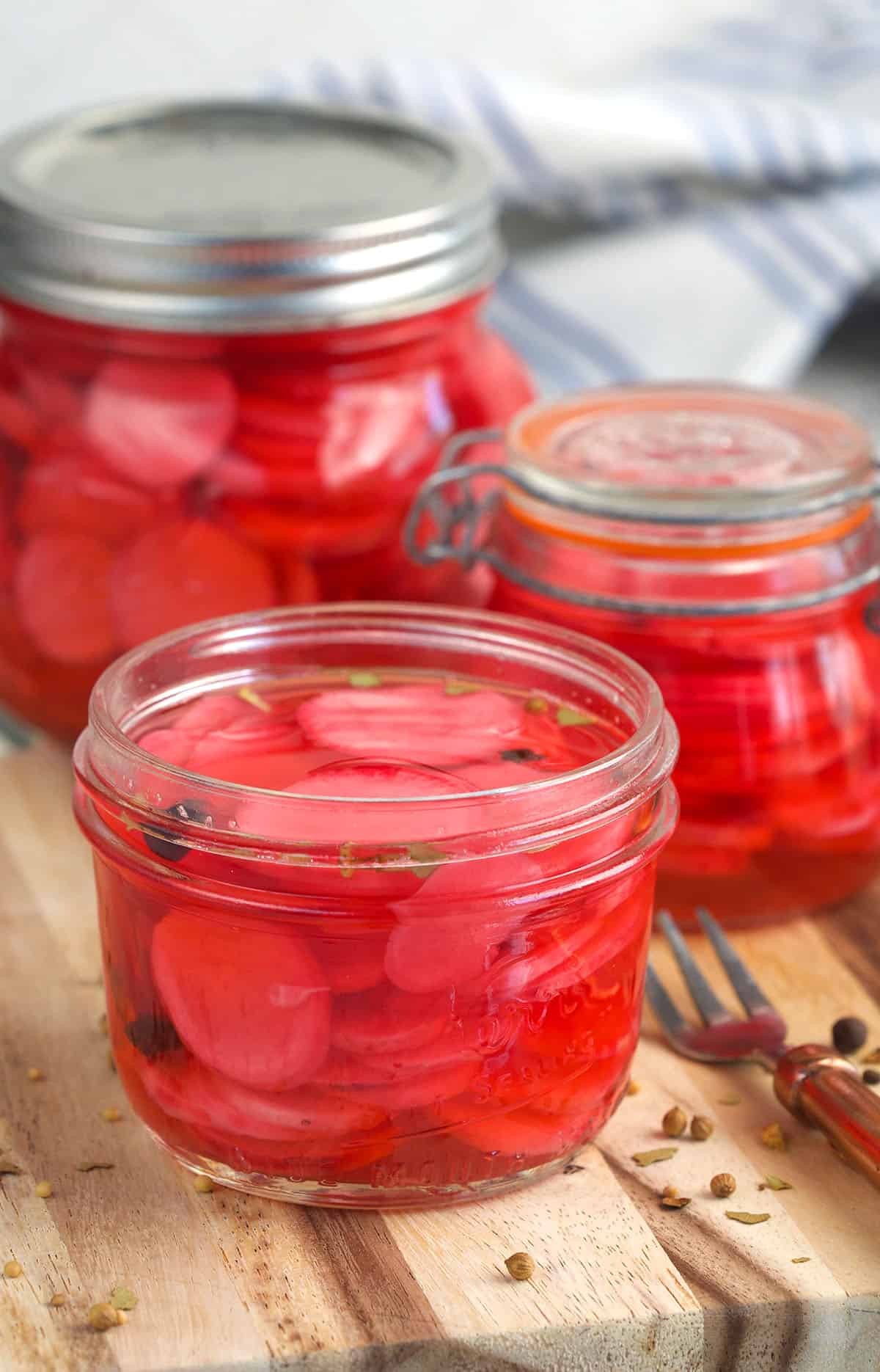Several jars of pickled radishes are placed on a wooden surface. 