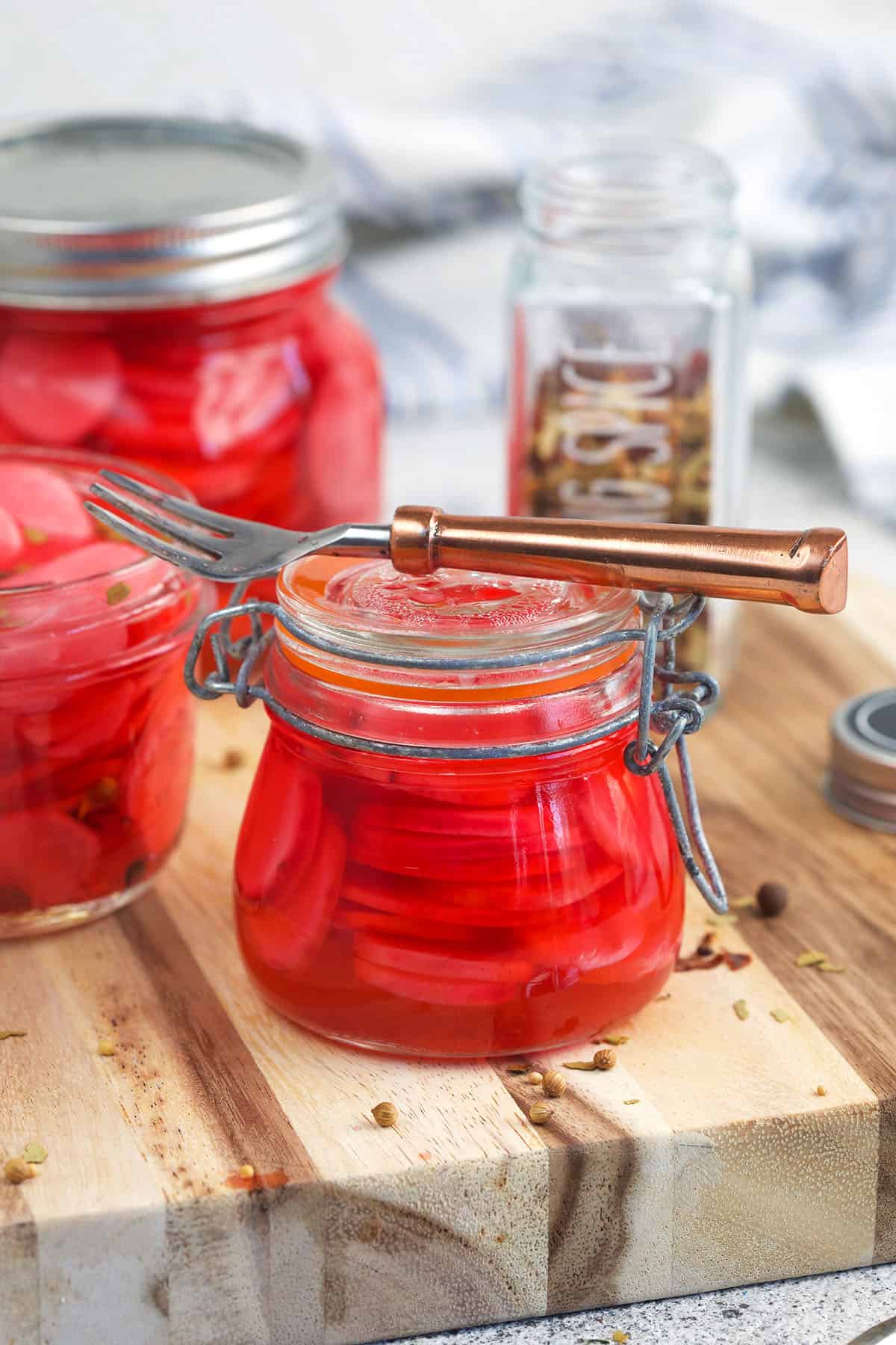 A small fork is placed on top of a jar filled with pickled radishes. 