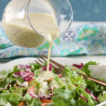Poppy seed dressing is being poured on top of salad.