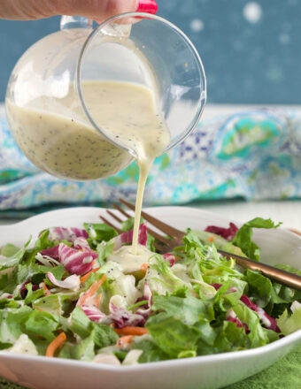 Poppy seed dressing is being poured on top of salad.