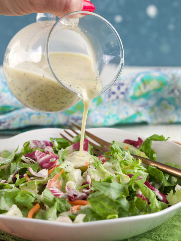 Poppy seed dressing is being poured on top of salad.
