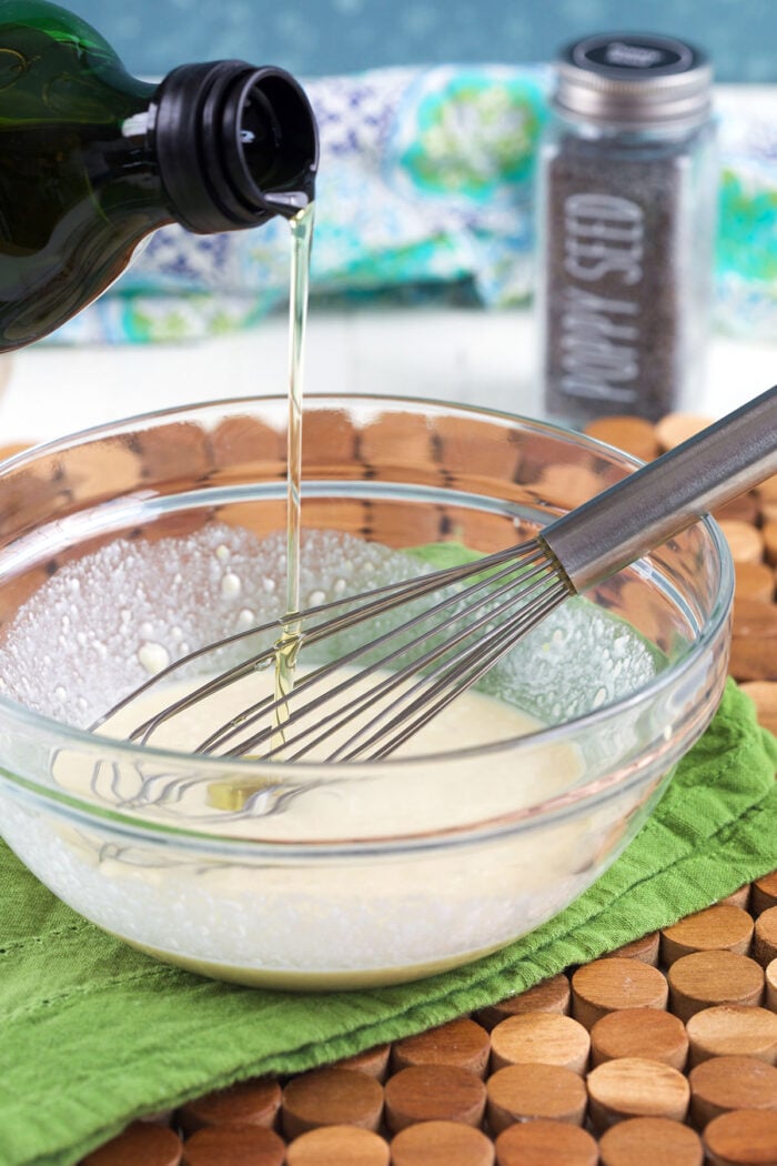 Oil is being drizzled into a bowl with a whisk.