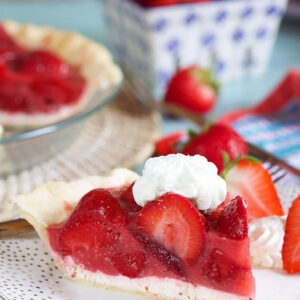 Slice of strawberry pie with whipped cream on a white plate with a fork.