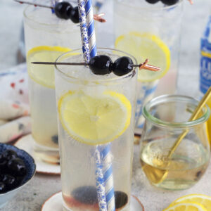 Blueberries and lemons garnish several glasses of tom collins.