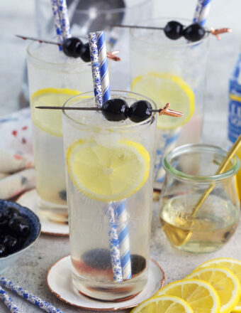 Blueberries and lemons garnish several glasses of tom collins.