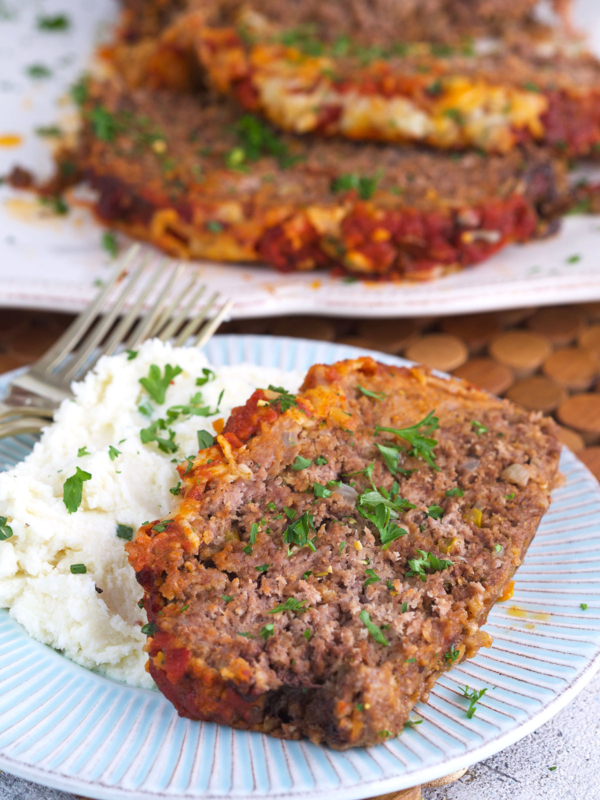 A garnished piece of meatloaf is on a plate with mashed potatoes.