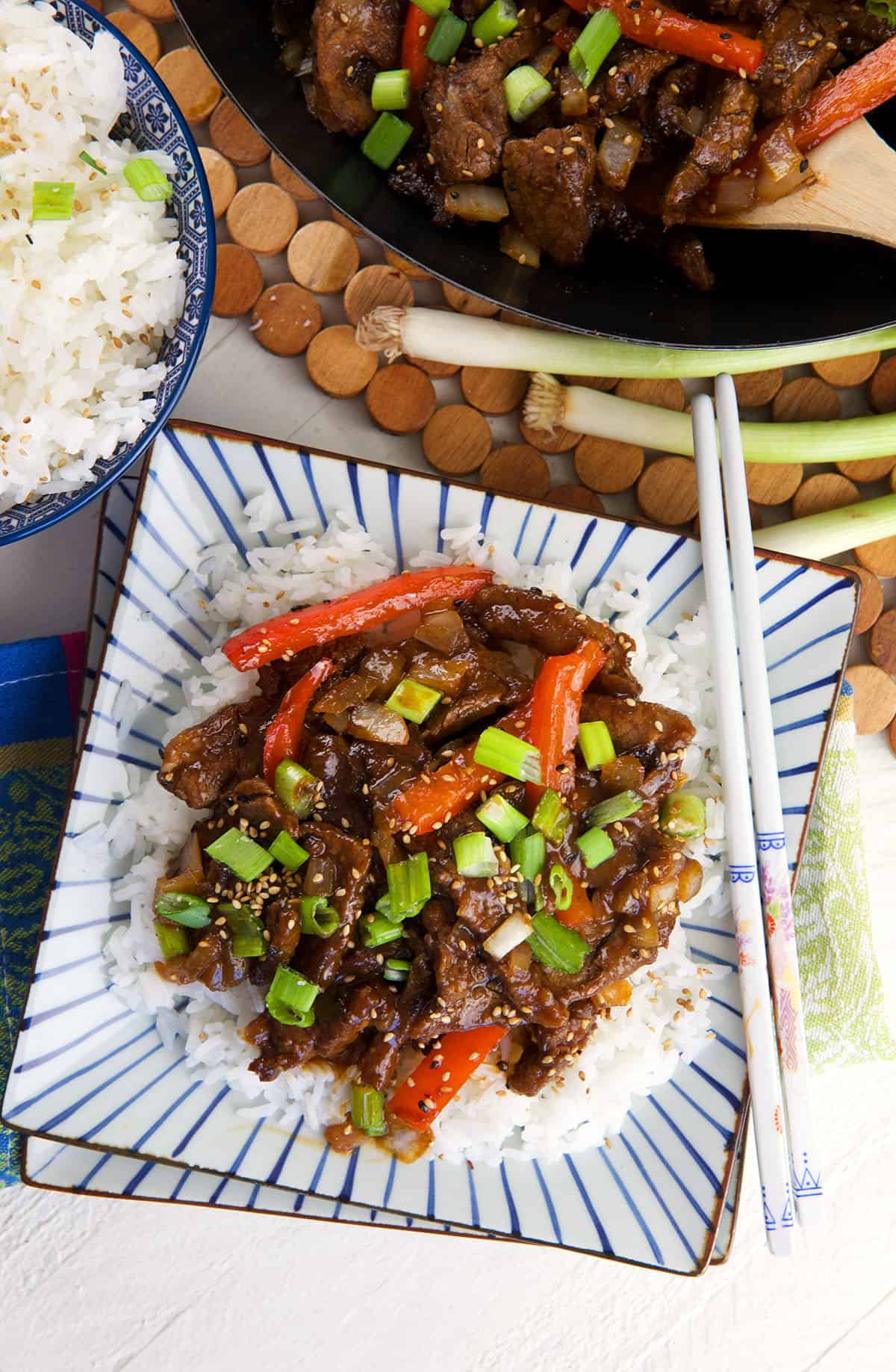 A pair of chopsticks are placed in a square plate with rice, beef and veggies. 