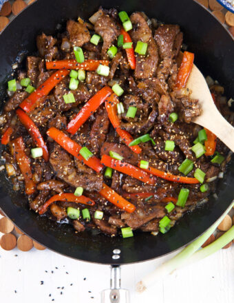 A wooden spoon is placed in a large skillet with Beijing beef.