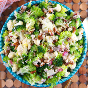 A blue serving bowl is filled with broccoli cauliflower salad.