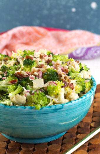 A blue serving bowl is filled with broccoli cauliflower salad.
