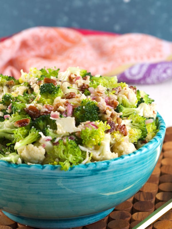 A blue serving bowl is filled with broccoli cauliflower salad.