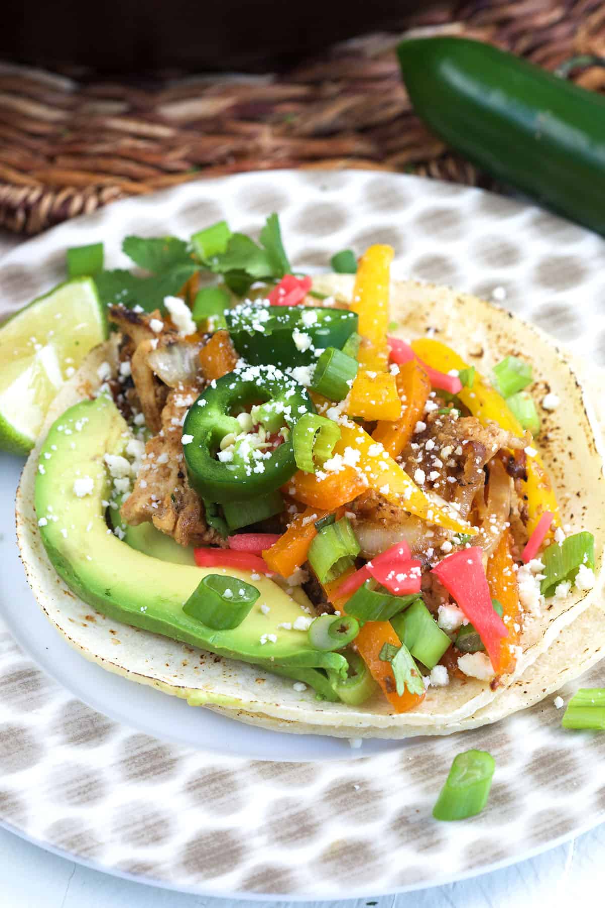A chicken fajita is topped with fresh veggies and cheese. 