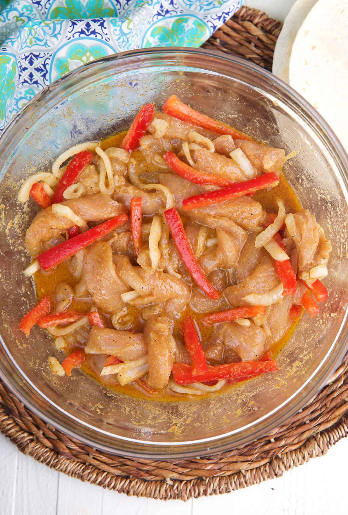 A glass bowl is filled with marinating chicken and veggies. 