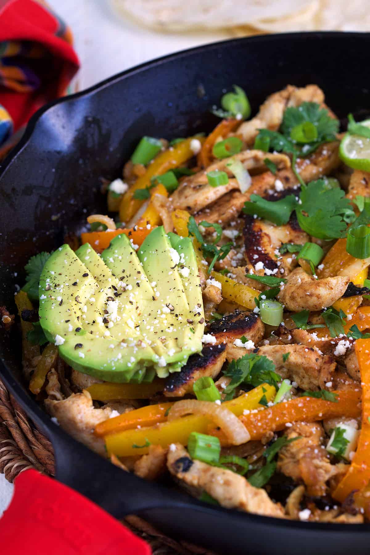 A sliced avocado is placed on top of a skillet of chicken fajitas. 