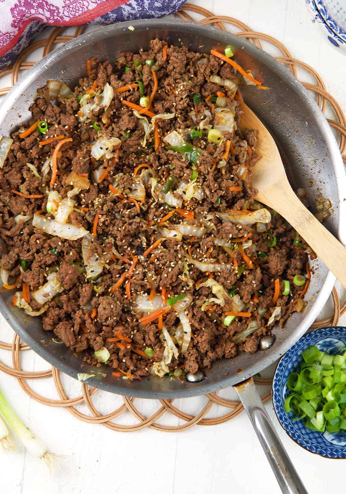 A wooden spoon is placed in a skillet filled with cooked ground beef and veggies. 