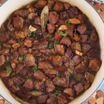 A pot of Filipino adobo is garnished with herbs.