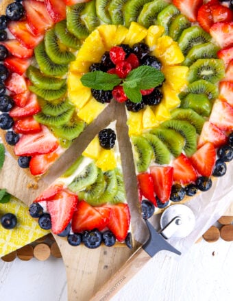 A slice of fruit pizza has been removed from the whole thing.