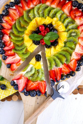 A slice of fruit pizza has been removed from the whole thing.