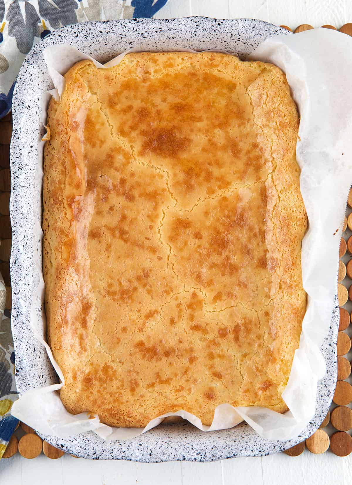 A baked cake is in a baking dish lined with parchment paper. 