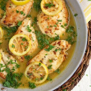 Several chicken breasts with lemons are presented in a skillet.