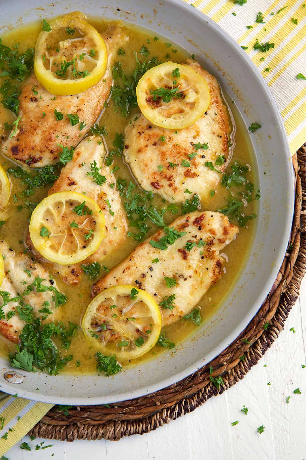 Several chicken breasts with lemons are presented in a skillet. 