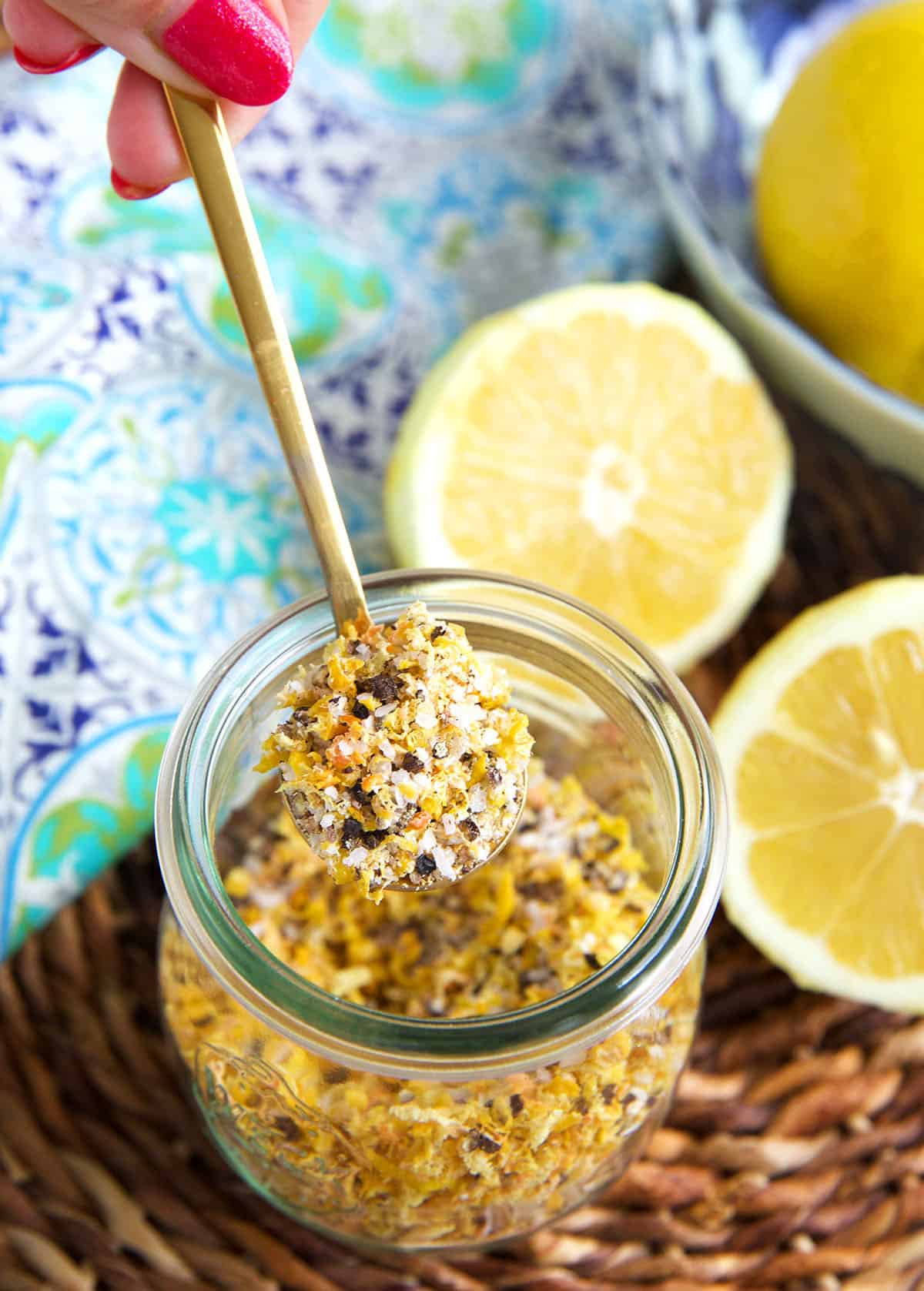 A small spoon is holding a portion of lemon pepper seasoning above a jar.