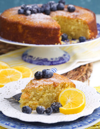 A slice of cake is presented with blueberries and lemons.