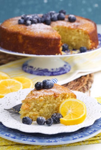 A slice of cake is presented with blueberries and lemons.