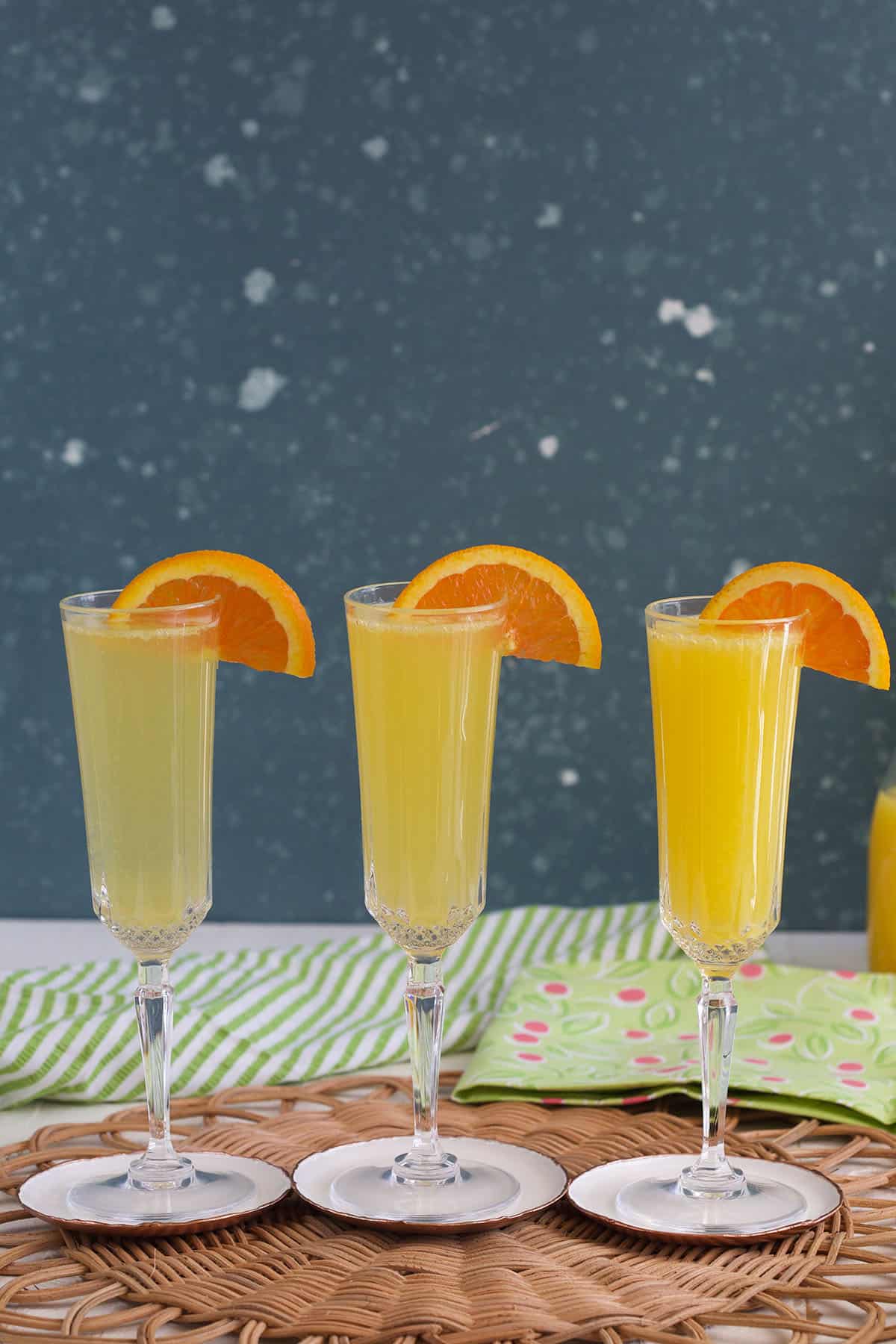 Three glasses of mimosas are placed on a brown place mat.