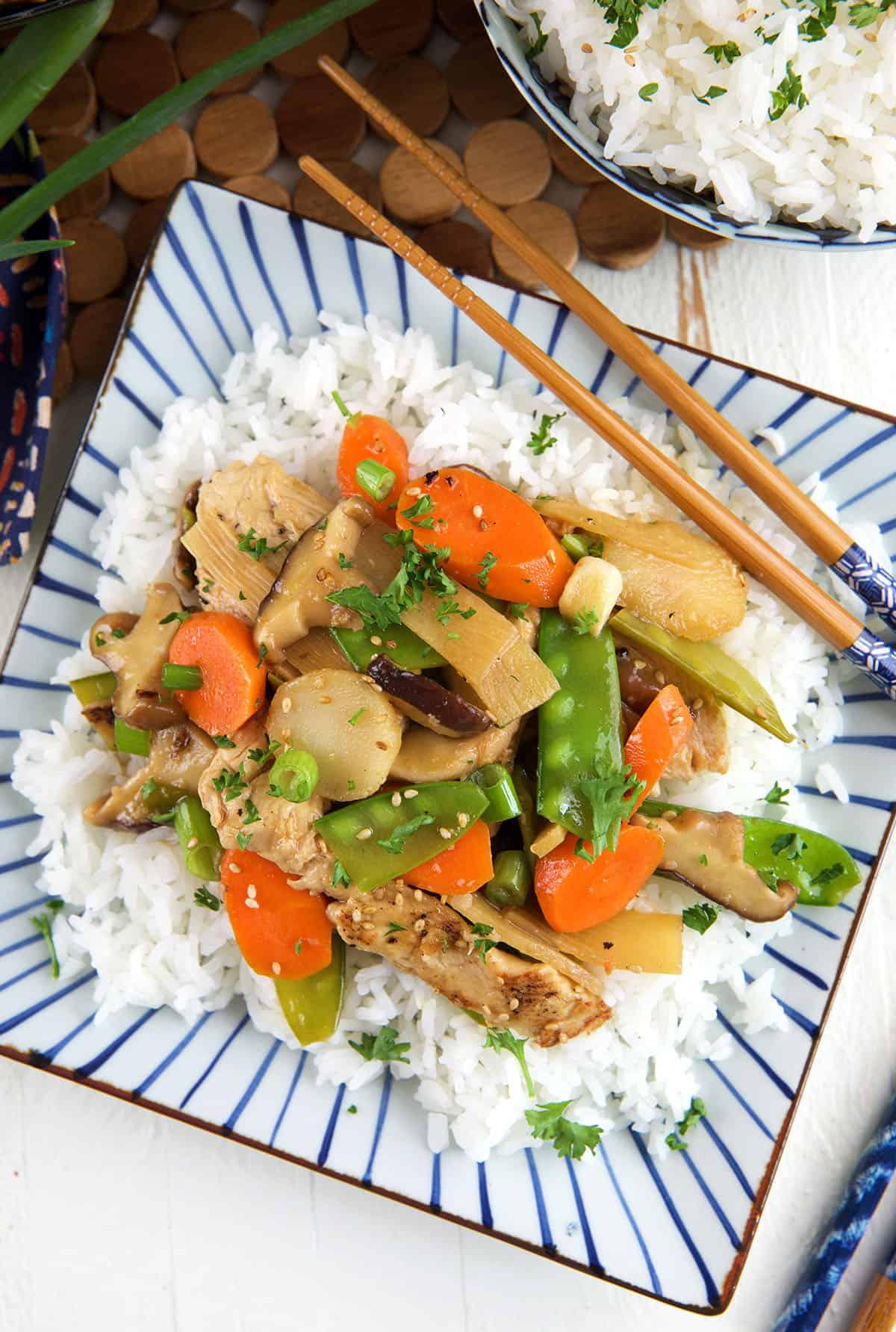 Rice, stir fry and chopsticks are placed on a striped plate. 