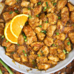 Slices of orange are placed in a skillet with orange chicken.