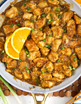 Slices of orange are placed in a skillet with orange chicken.