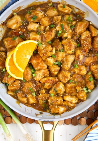 Slices of orange are placed in a skillet with orange chicken.