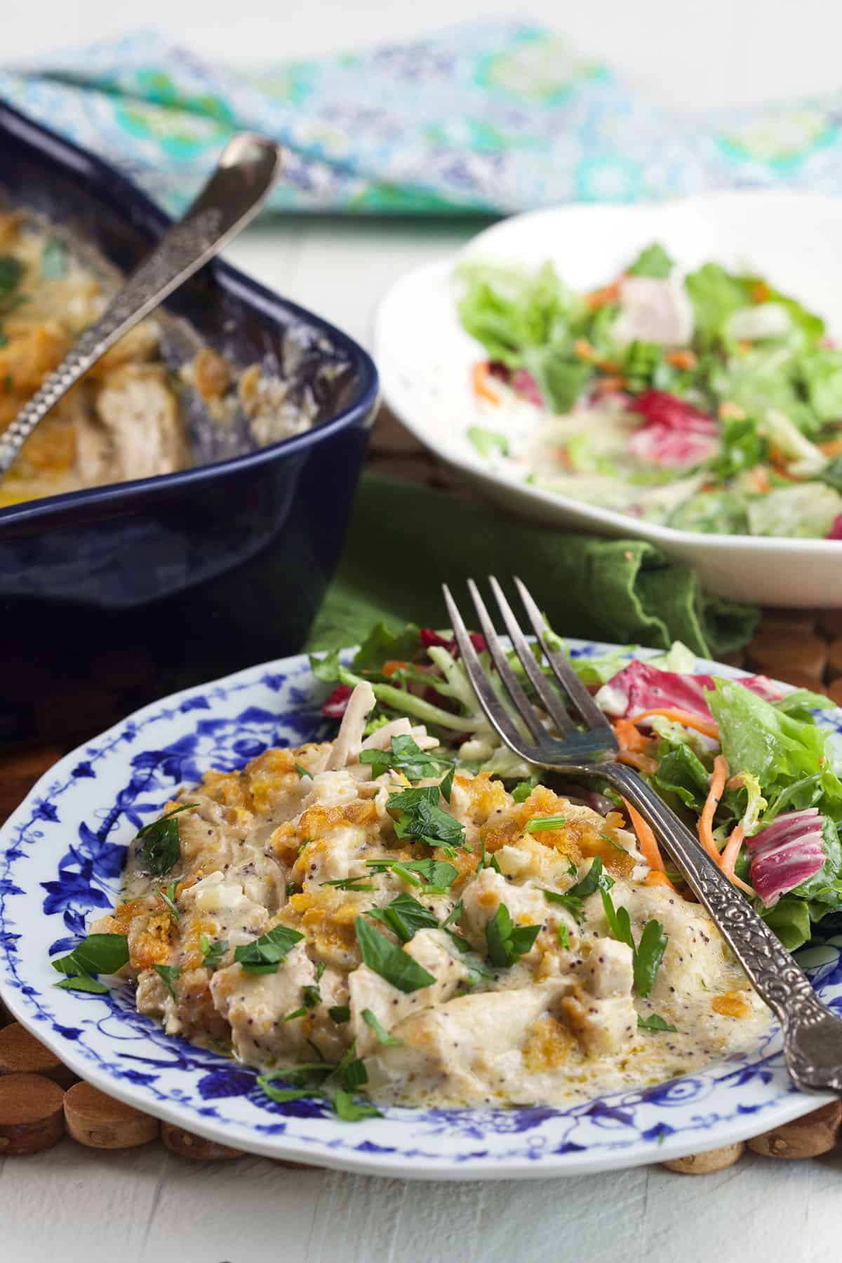 A plate topped with salad and poppy seed chicken is presented with a fork. 
