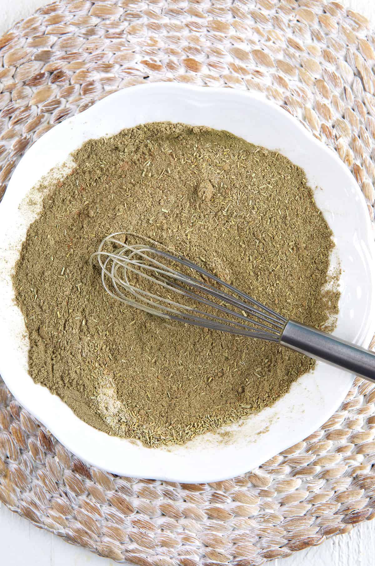 A whisk is combining poultry seasoning in a shallow bowl. 