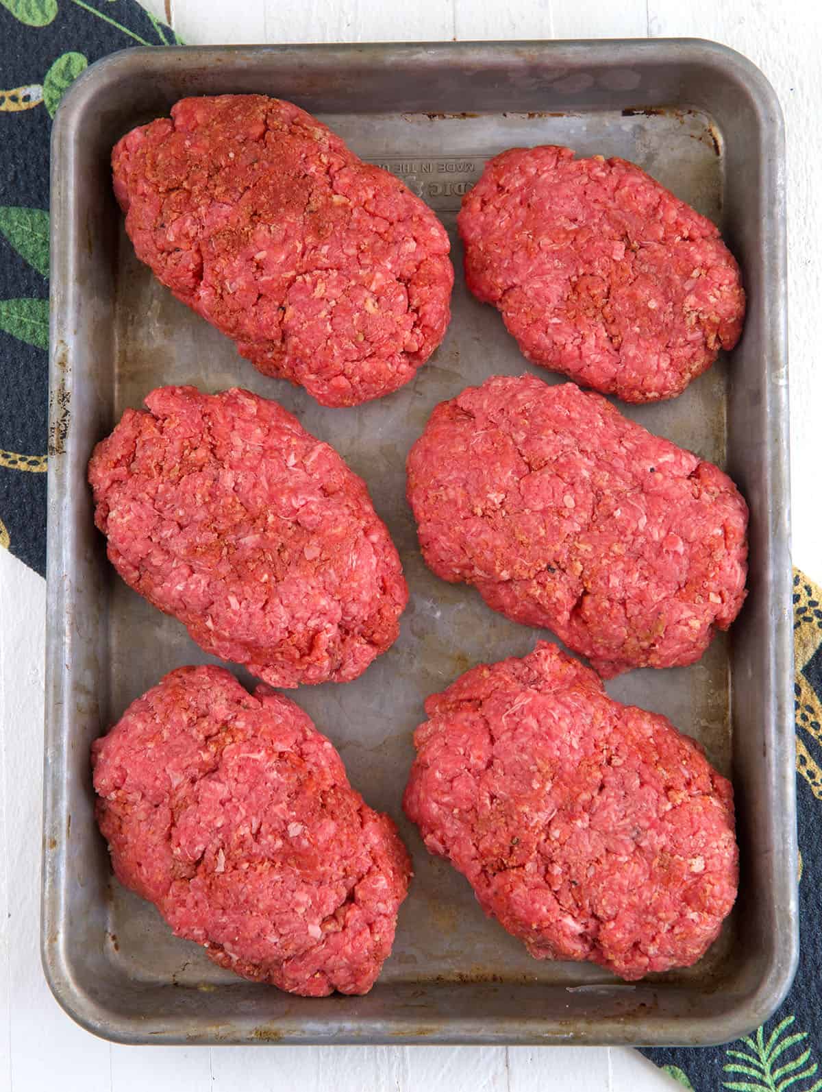 Ground beef formed into oval patties for Salisbury Steak on a baking sheet.
