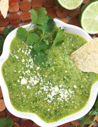 A chip is placed in a bowl of salsa verde.