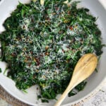 A spoon is placed in a skillet filled with sautéed spinach.