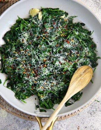 A spoon is placed in a skillet filled with sautéed spinach.